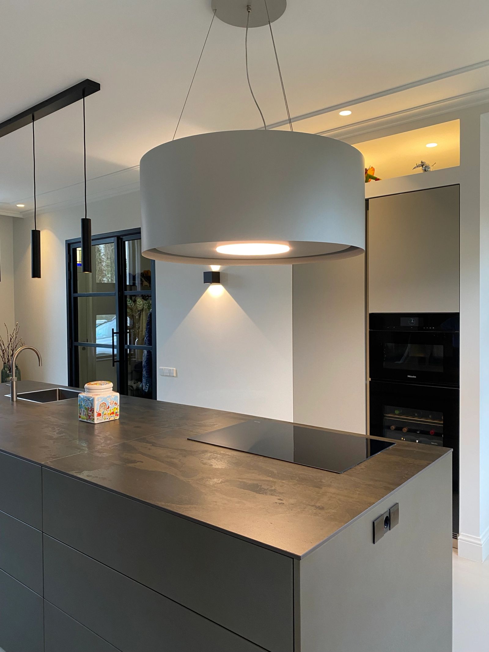 Olijfgrijze hoge kasten met Miele ovens naast het greeploze eiland