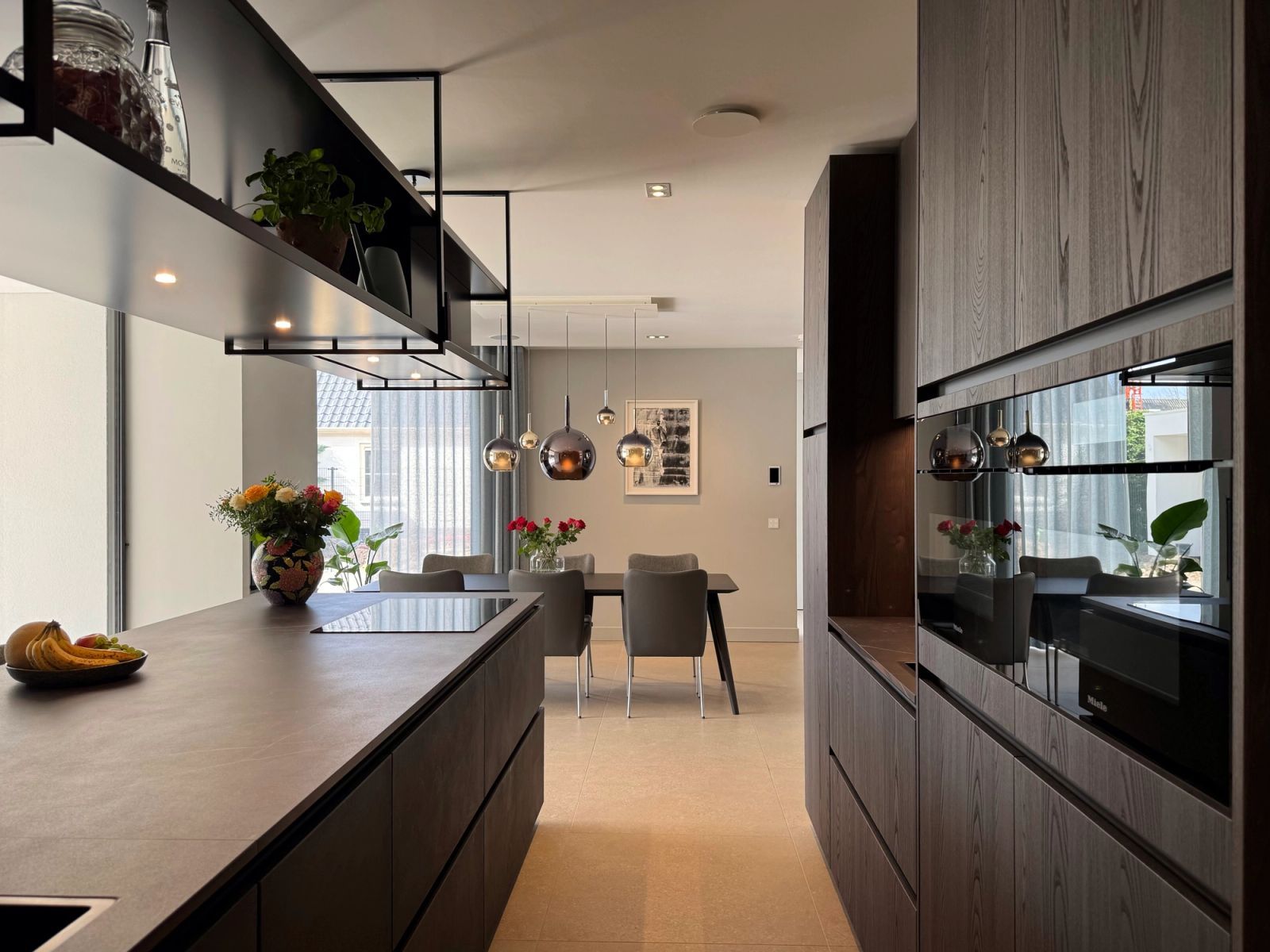 Betonnen kookeiland met inductie naast de iepenhouten kastenwand met Miele inbouw