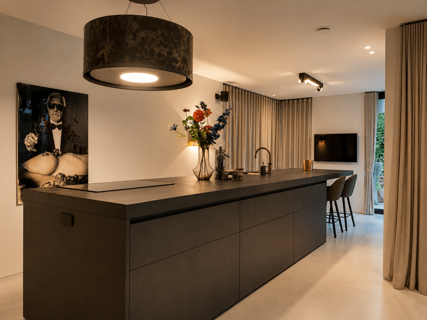 Maatwerk designkeuken met een robuust donker kookeiland, een leren afzuigkap en een taupegrijze Fenix-kastenwand, geleverd door Wildhagen