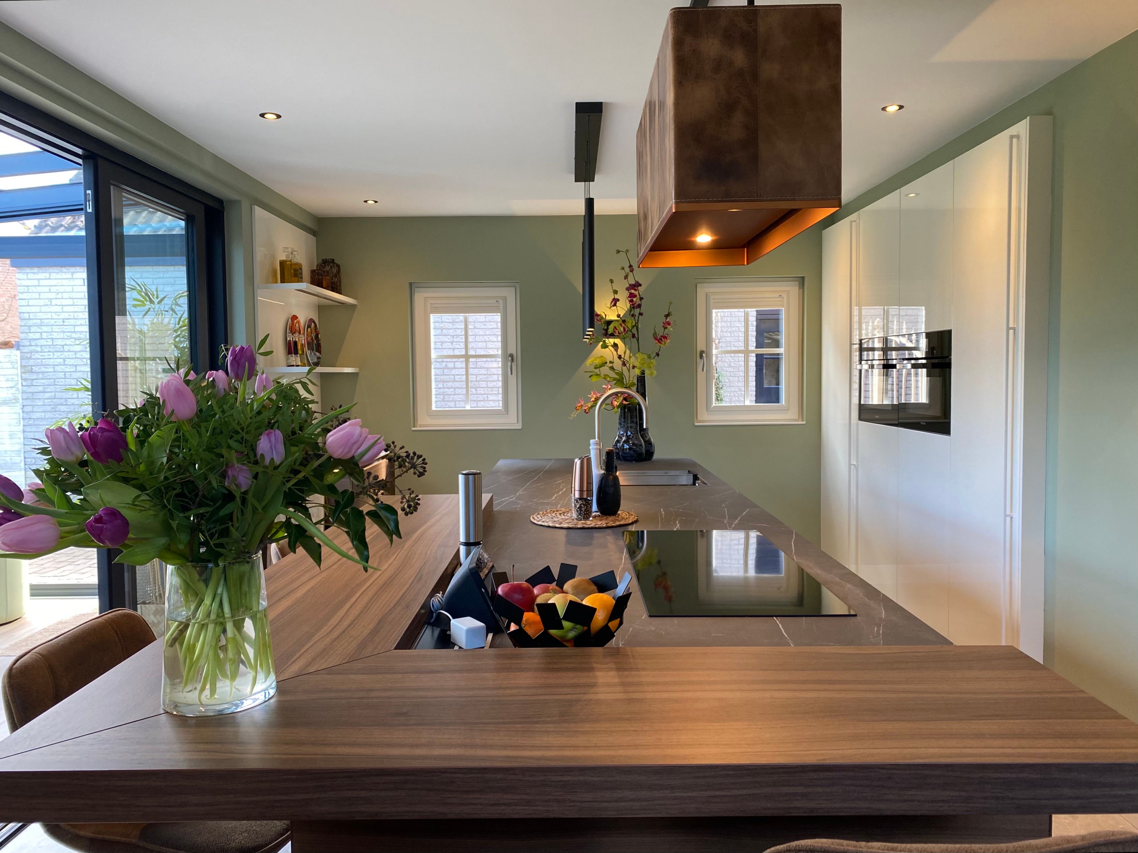 Zicht over het eiland naar de hoogglans witte kastenwand met Miele inbouw