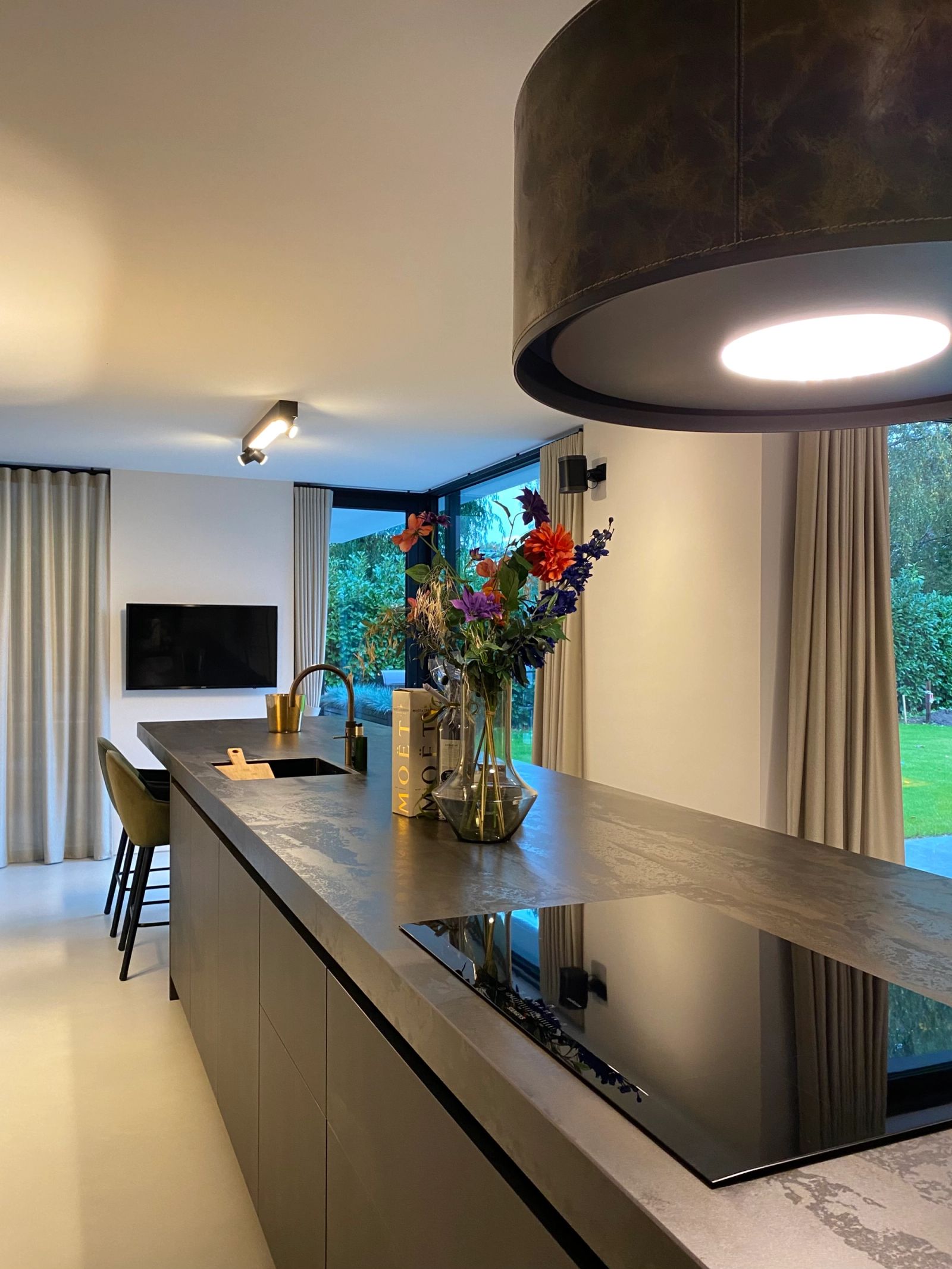 Robuust kookeiland met dik Dekton-werkblad in Radium onder de leren afzuigkap